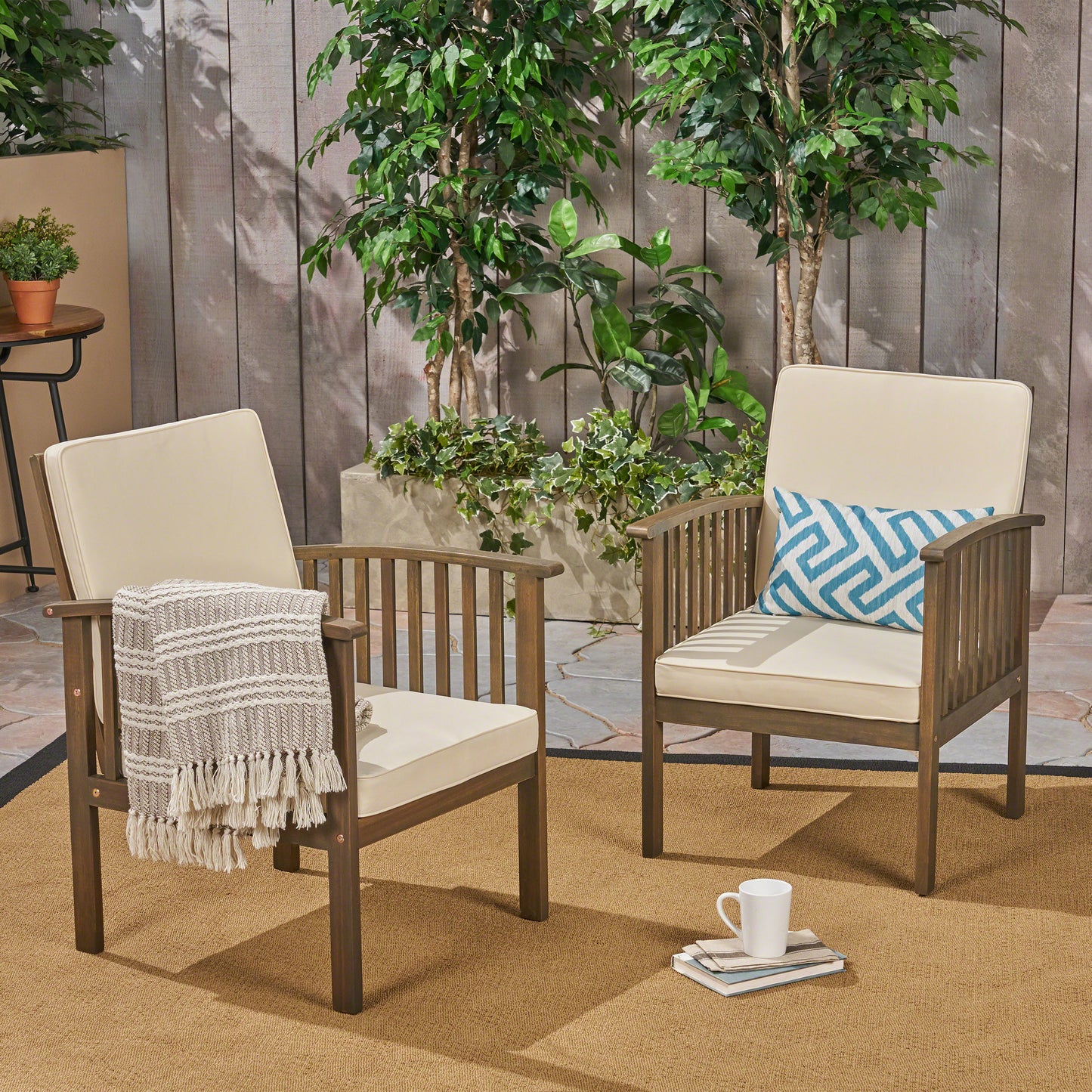 Two dark wood patio chairs with cream cushions and a blue patterned accent pillow