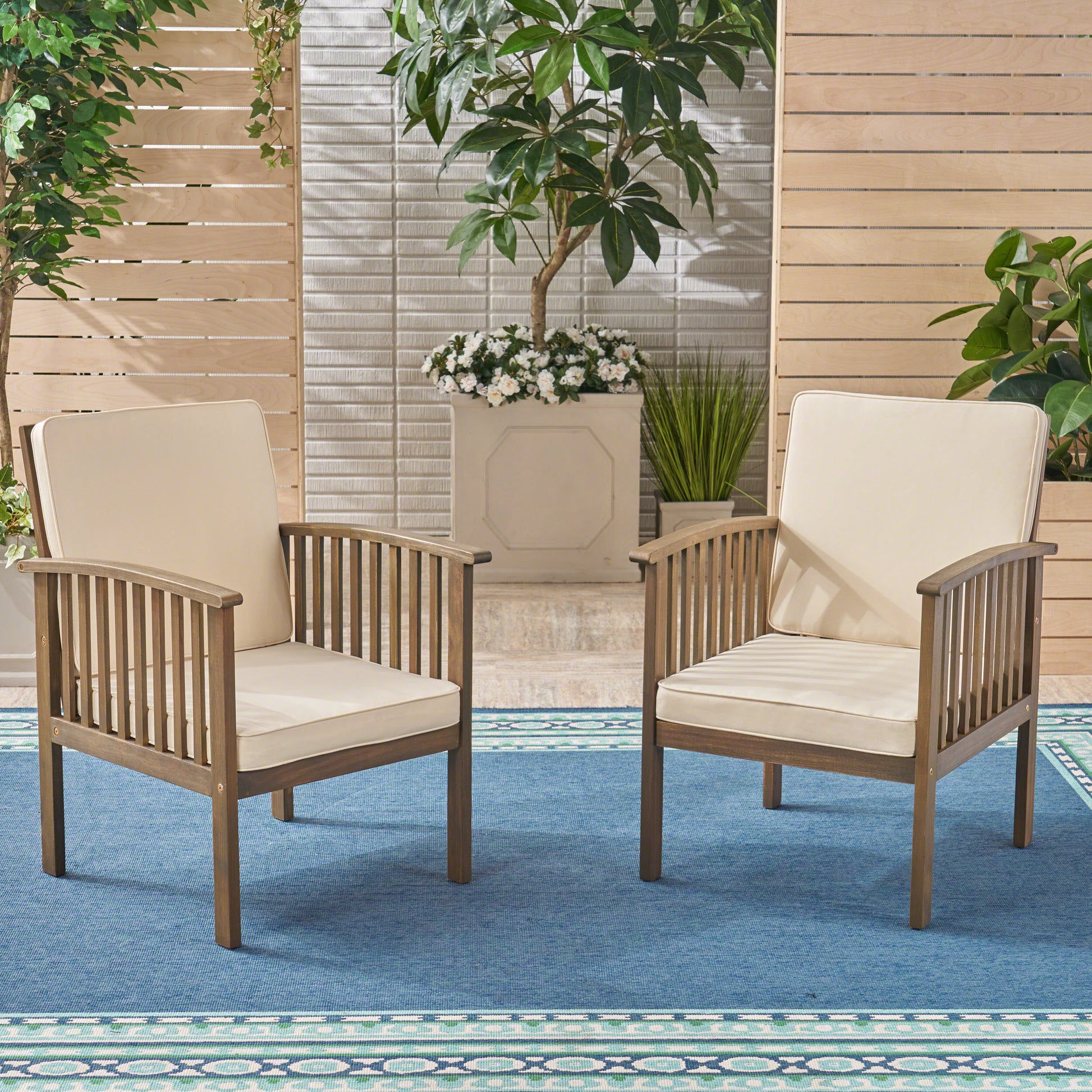 Two wooden outdoor armchairs with cream cushions set on a blue patio rug