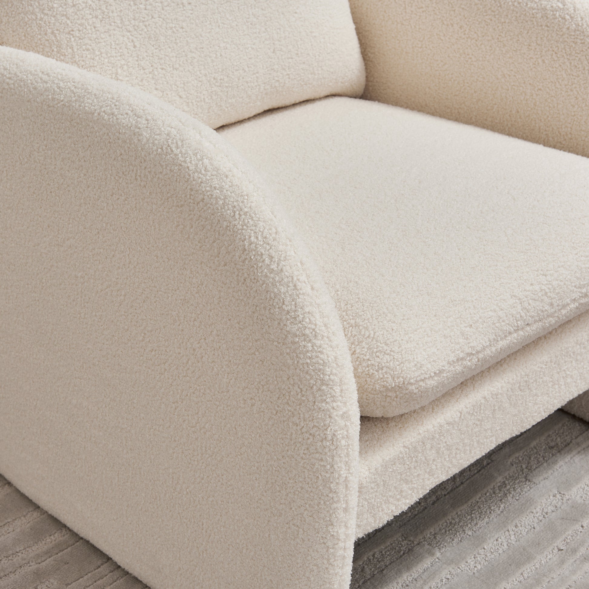Plush cream boucle armchair closeup showing textured fabric and curved armrest detail