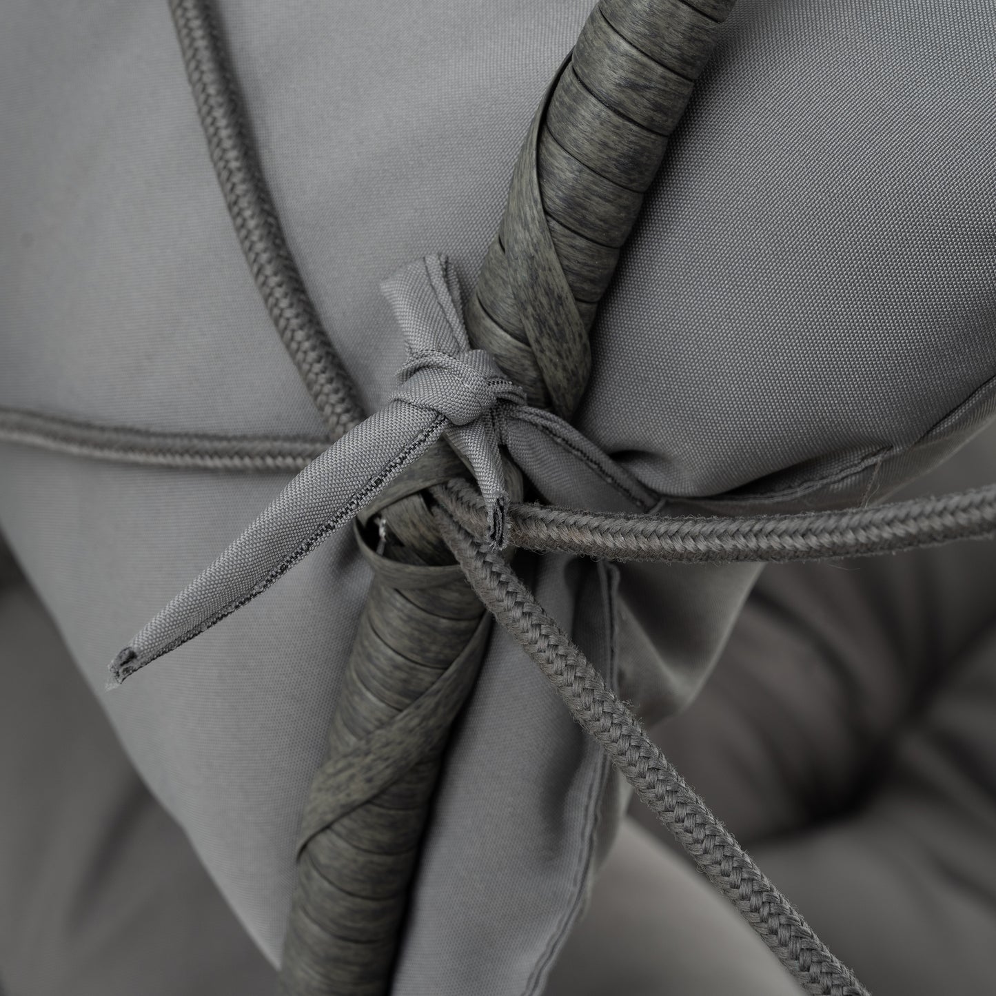 Closeup of a braided grey cord tied to a textured grey rattan frame on an outdoor cushion