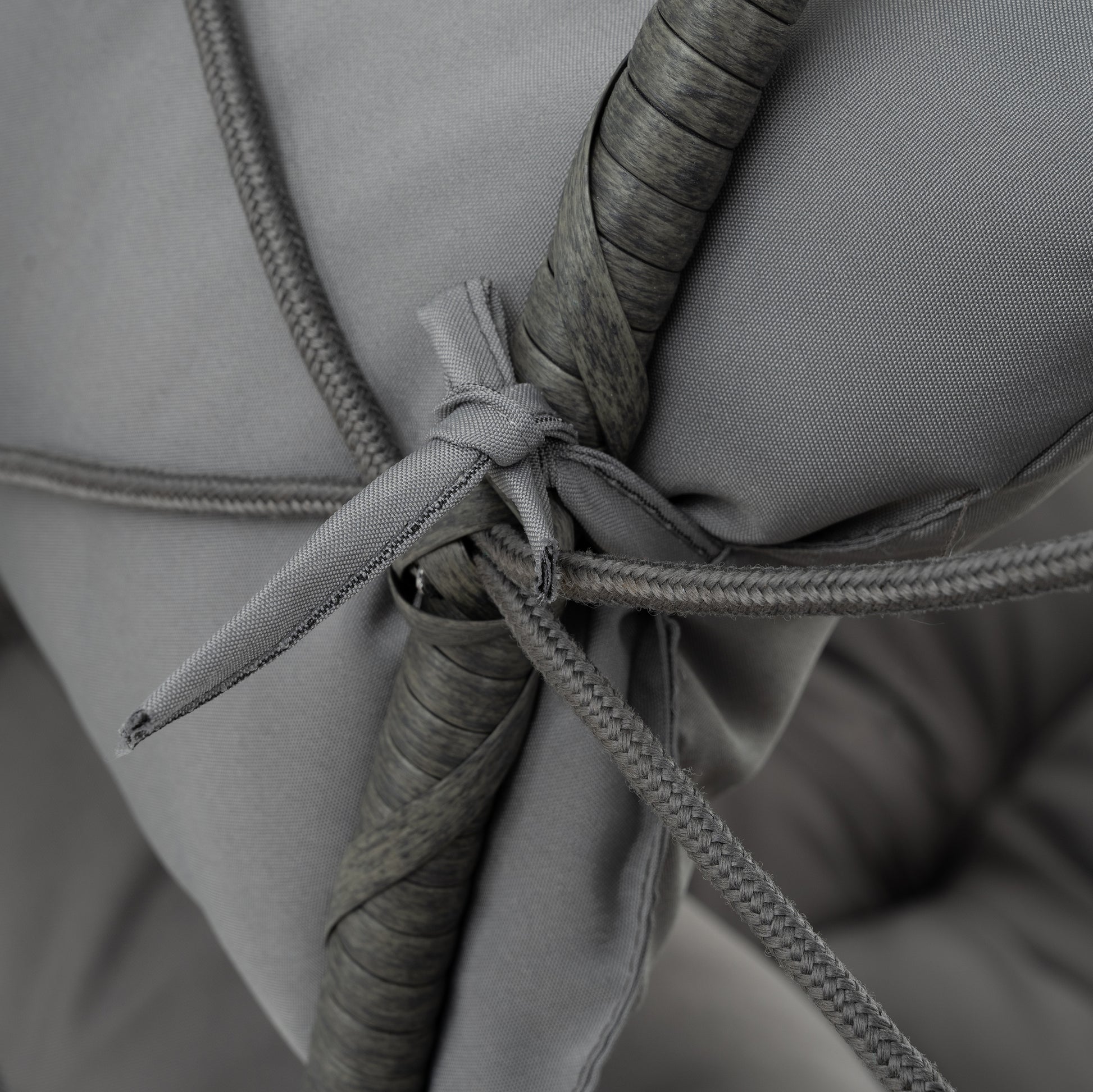 Closeup of a braided grey cord tied to a textured grey rattan frame on an outdoor cushion