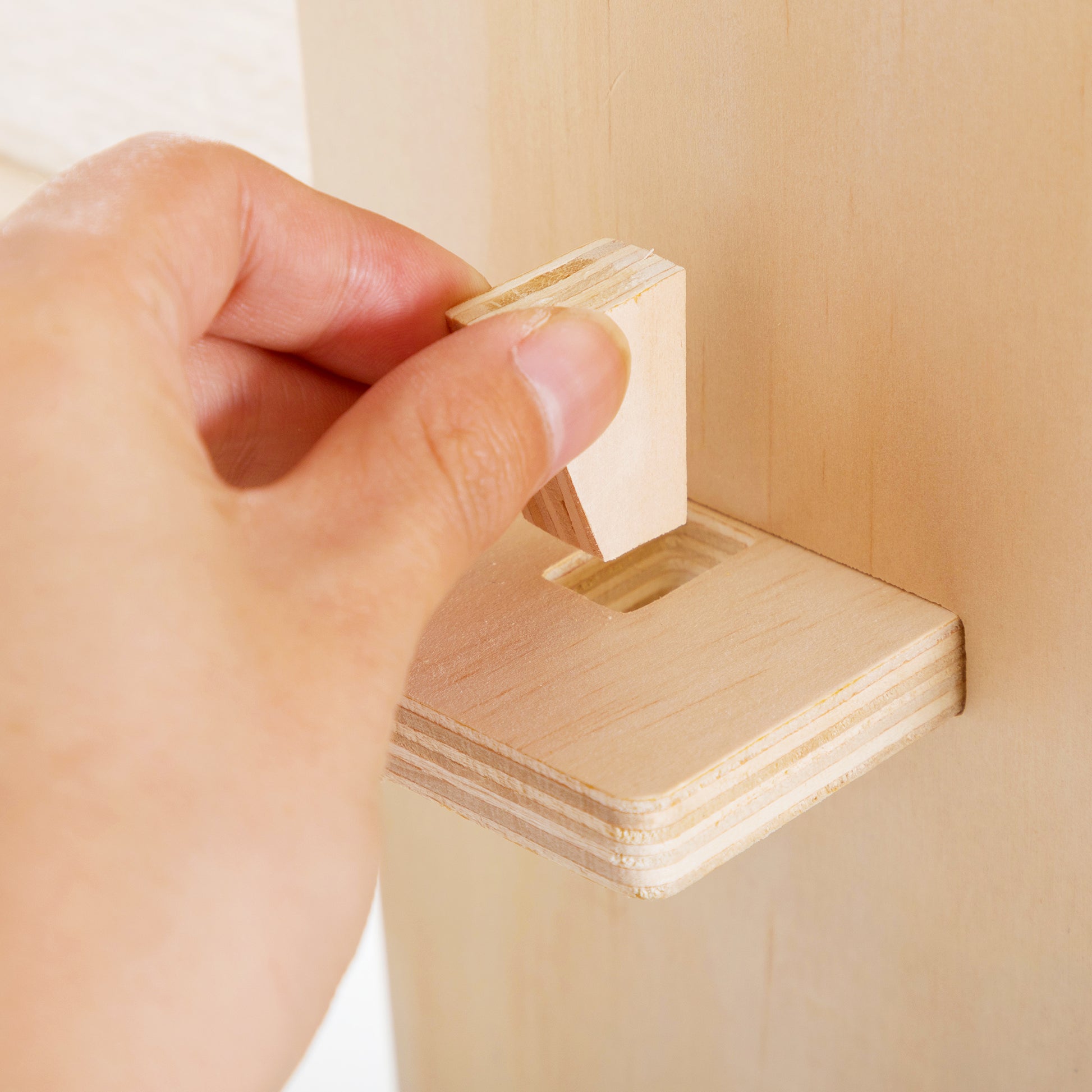 Hand inserting wooden dowel into unfinished plywood furniture joint for assembly