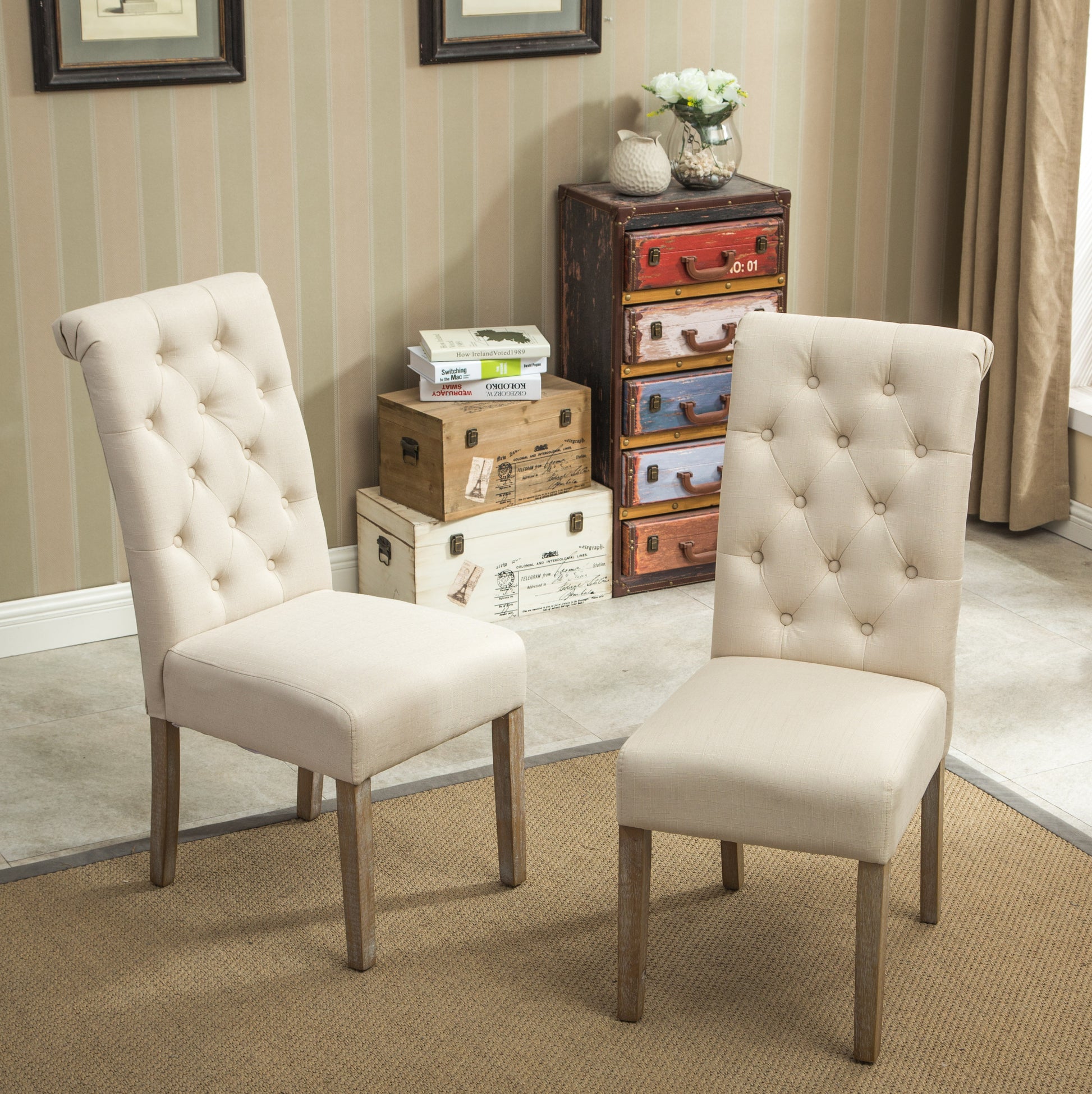 Two beige linen dining chairs with button tufting on the back and weathered wood legs