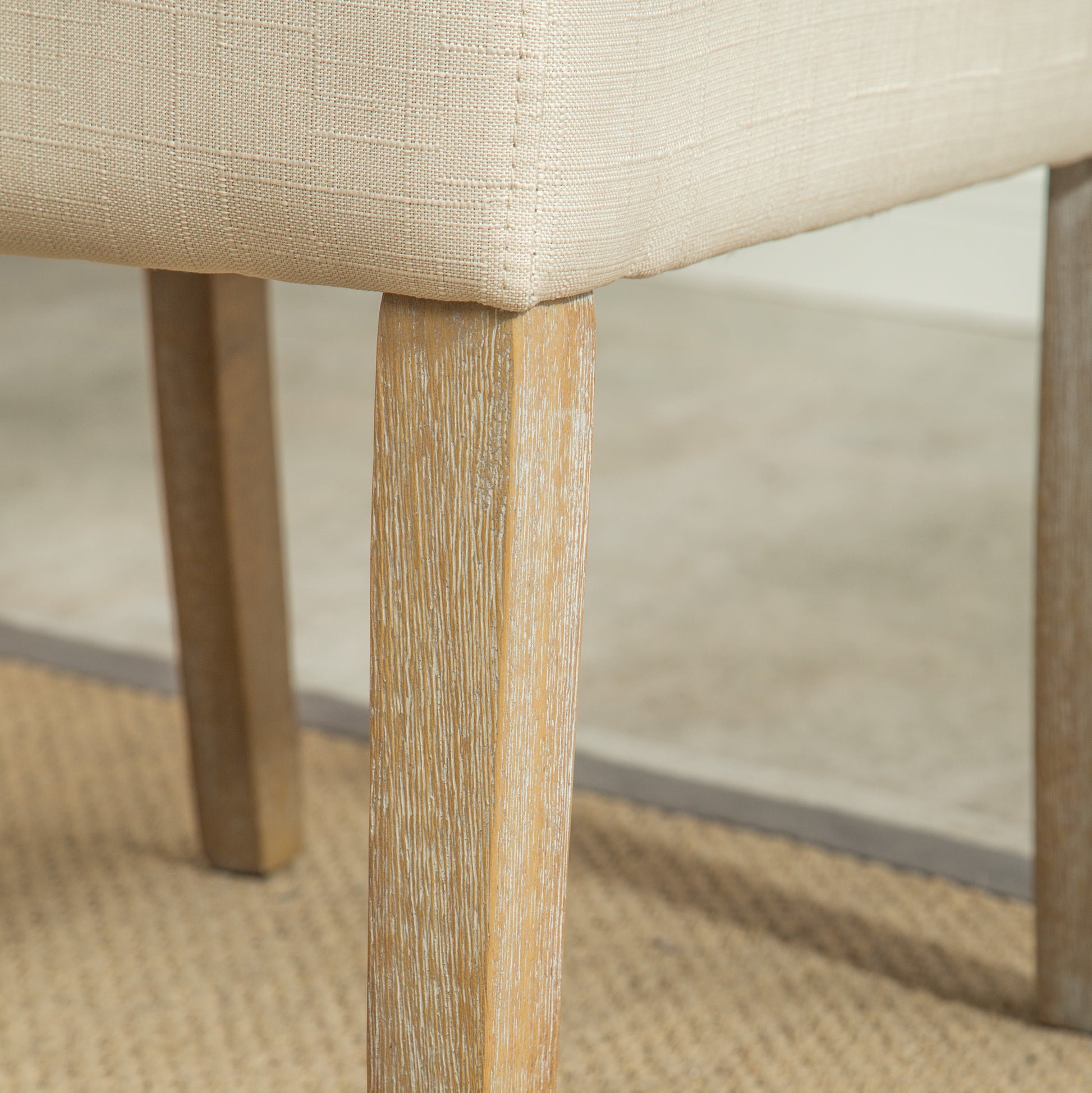 Closeup of a beige linen upholstered chair leg with a weathered wood finish