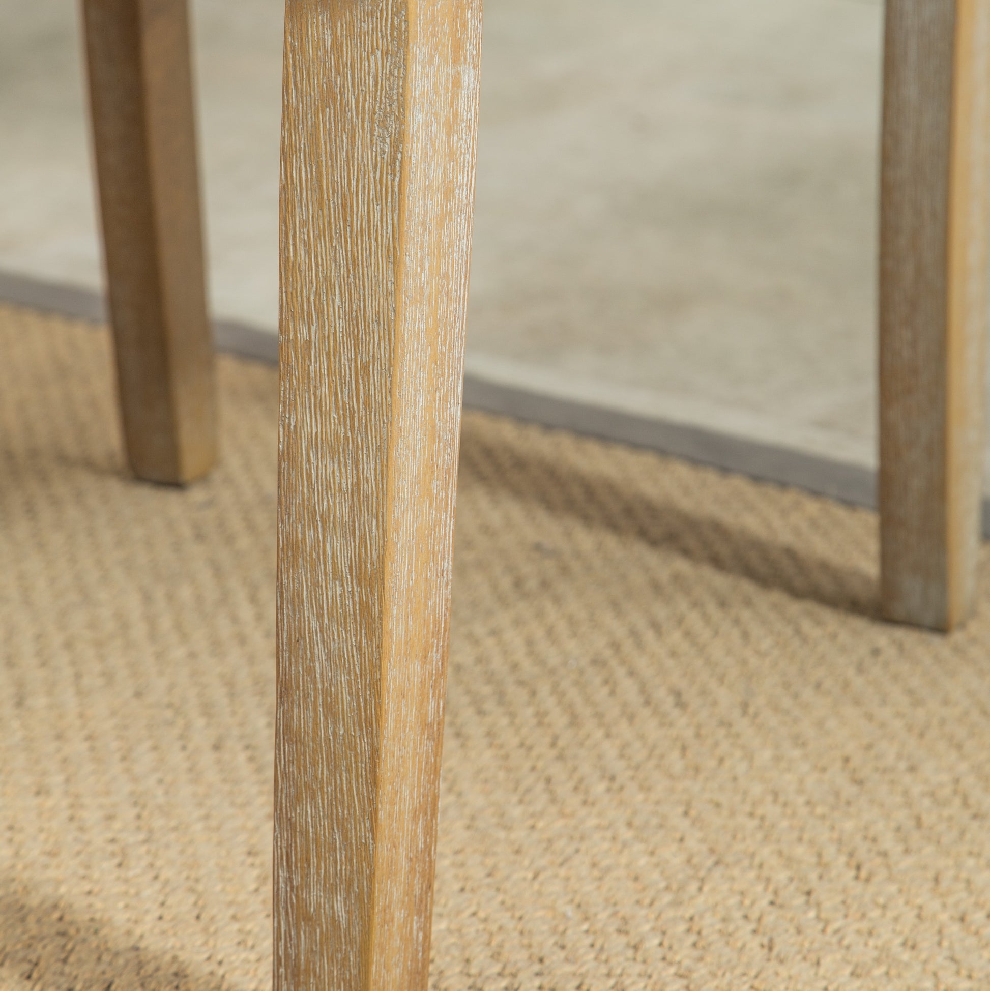 Closeup of a weathered oak wood table leg with a distressed finish on a woven rug