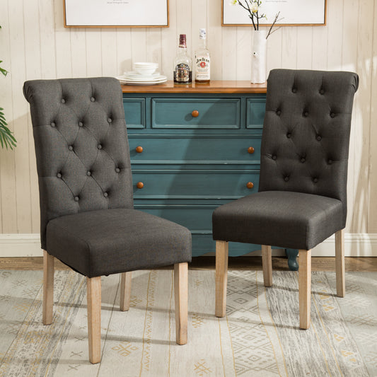 Two upholstered dining chairs in charcoal grey fabric with tufted backs and light wood legs