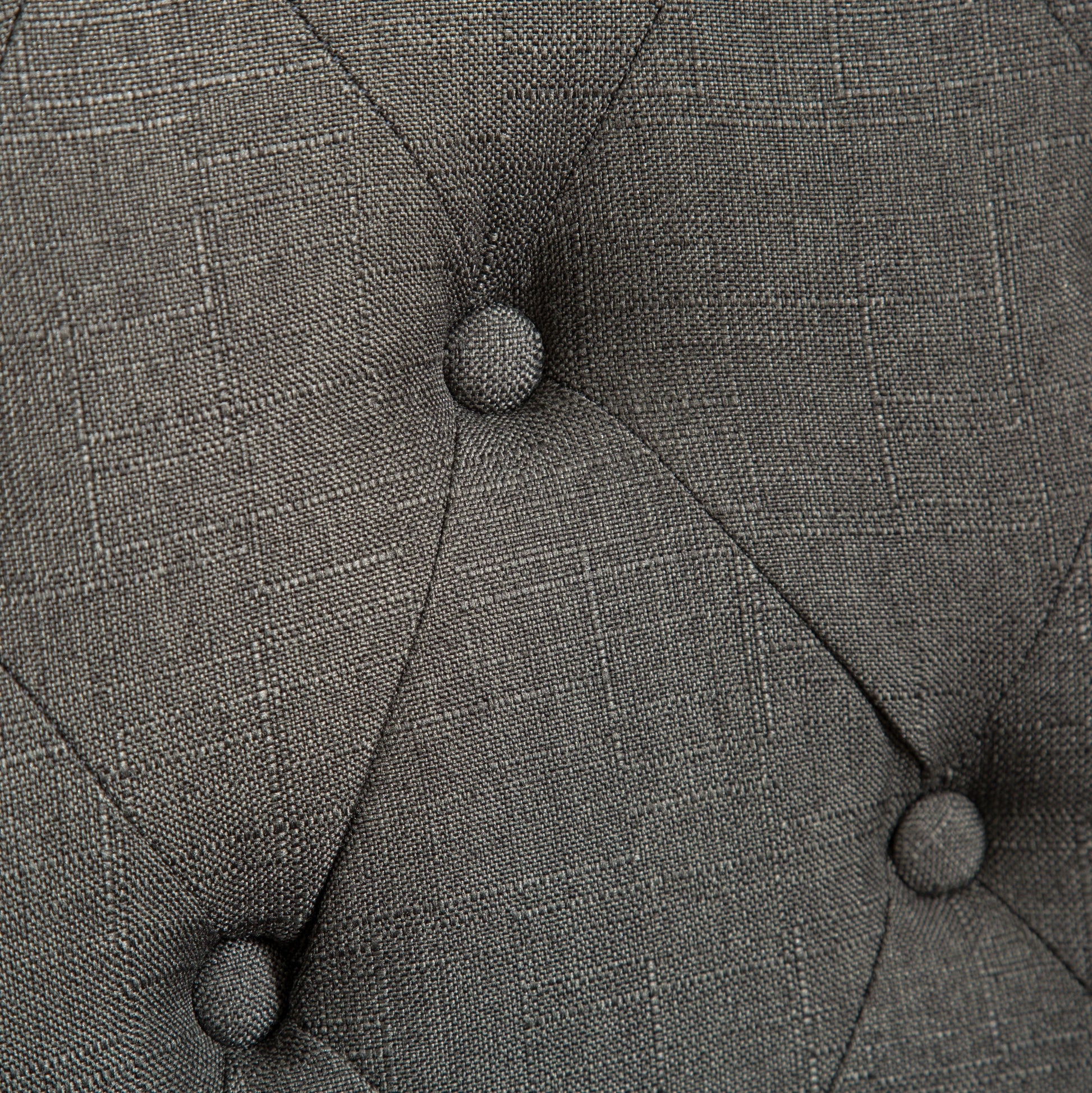 Closeup of tufted dark grey fabric with diamond pattern stitching showcasing textile texture