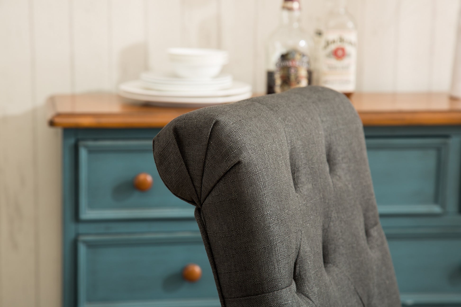Charcoal gray tufted dining chair with textured fabric upholstery and wooden knobs on blue dresser