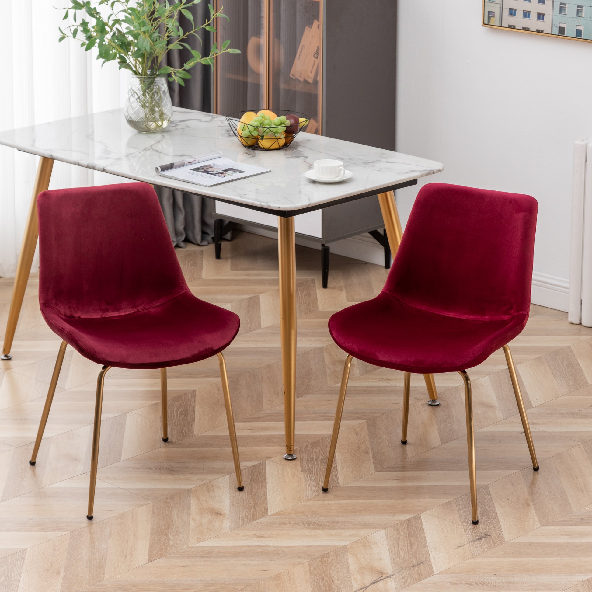 Two plush velvet dining chairs in deep red with elegant gold metal legs