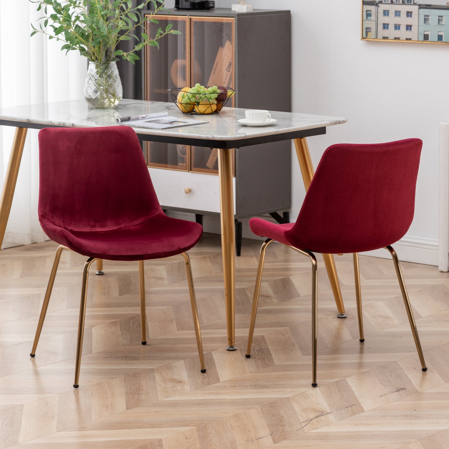 Two plush velvet dining chairs in deep red with sleek gold legs