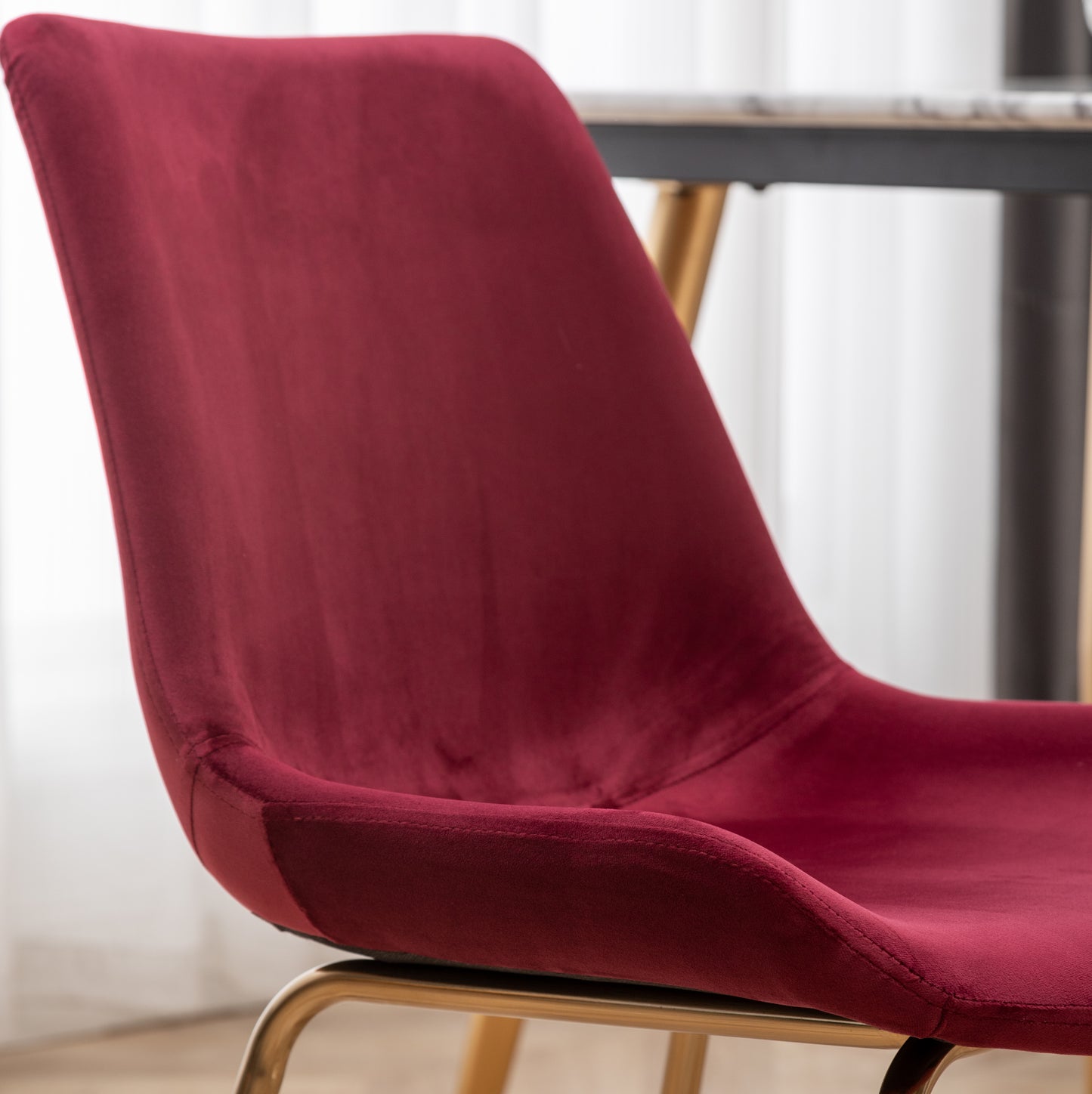 Closeup of a plush burgundy velvet chair with sleek gold metal legs perfect for a modern dining room