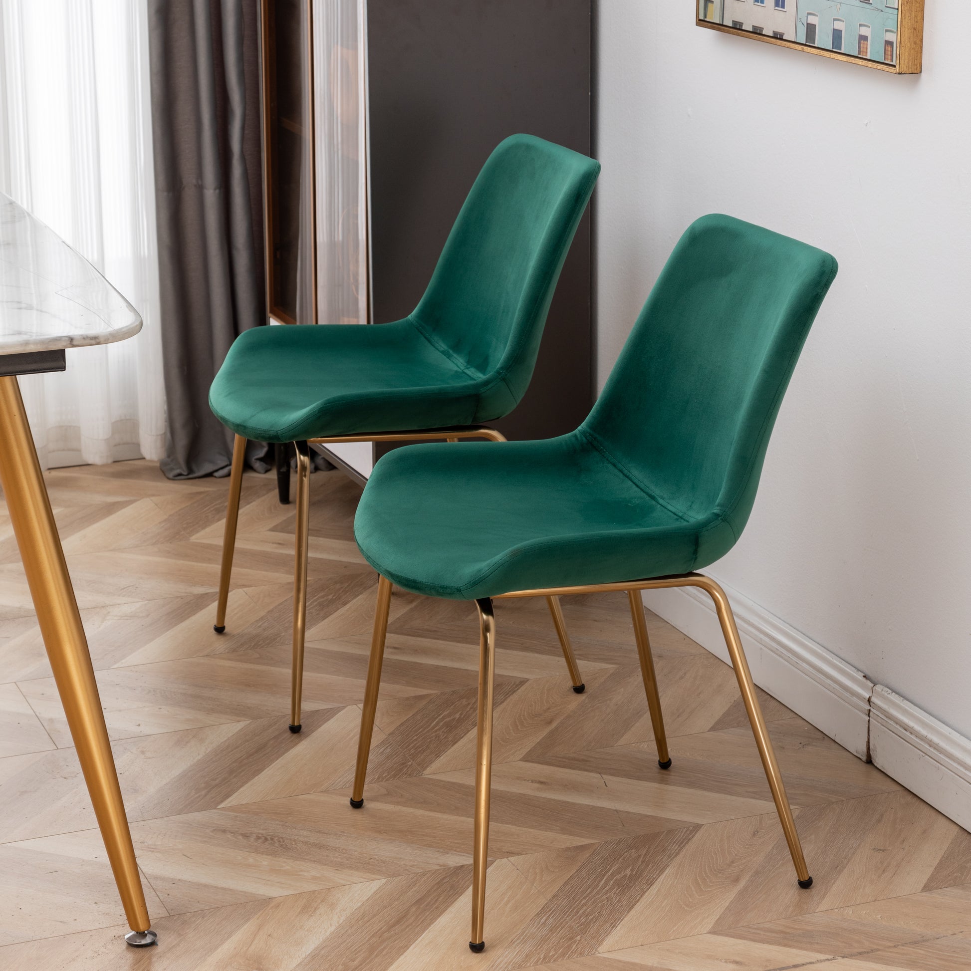 Two plush emerald green velvet dining chairs with gold metal legs