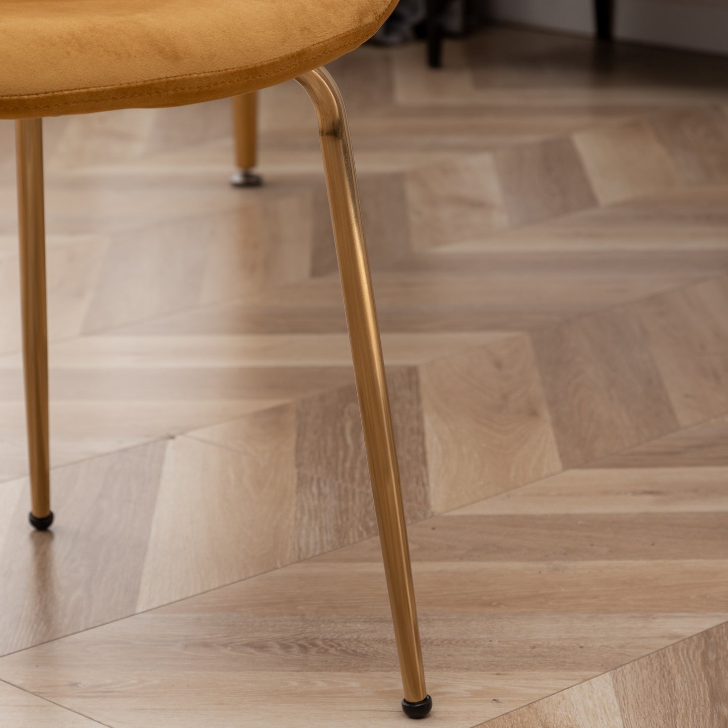 Gold metal leg of a mustard velvet dining chair on a wood parquet floor