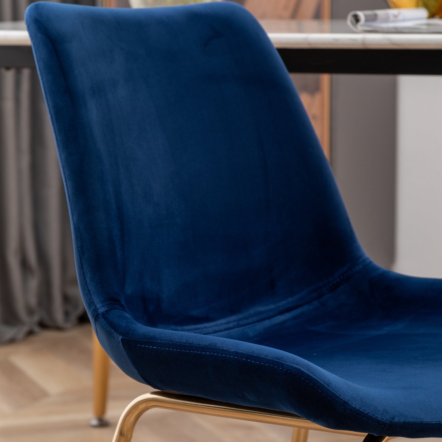 Closeup of a deep blue velvet dining chair with gold metal legs