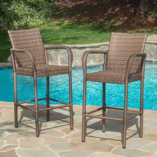 Two brown wicker bar stools with arms positioned by a swimming pool perfect for outdoor seating