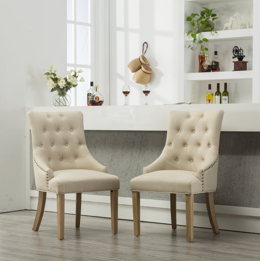 Two tufted beige dining chairs with nailhead trim and wooden legs