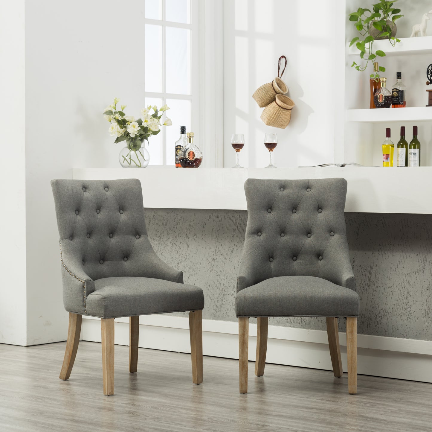 Two grey linen tufted dining chairs with brass nailhead trim and natural wood legs