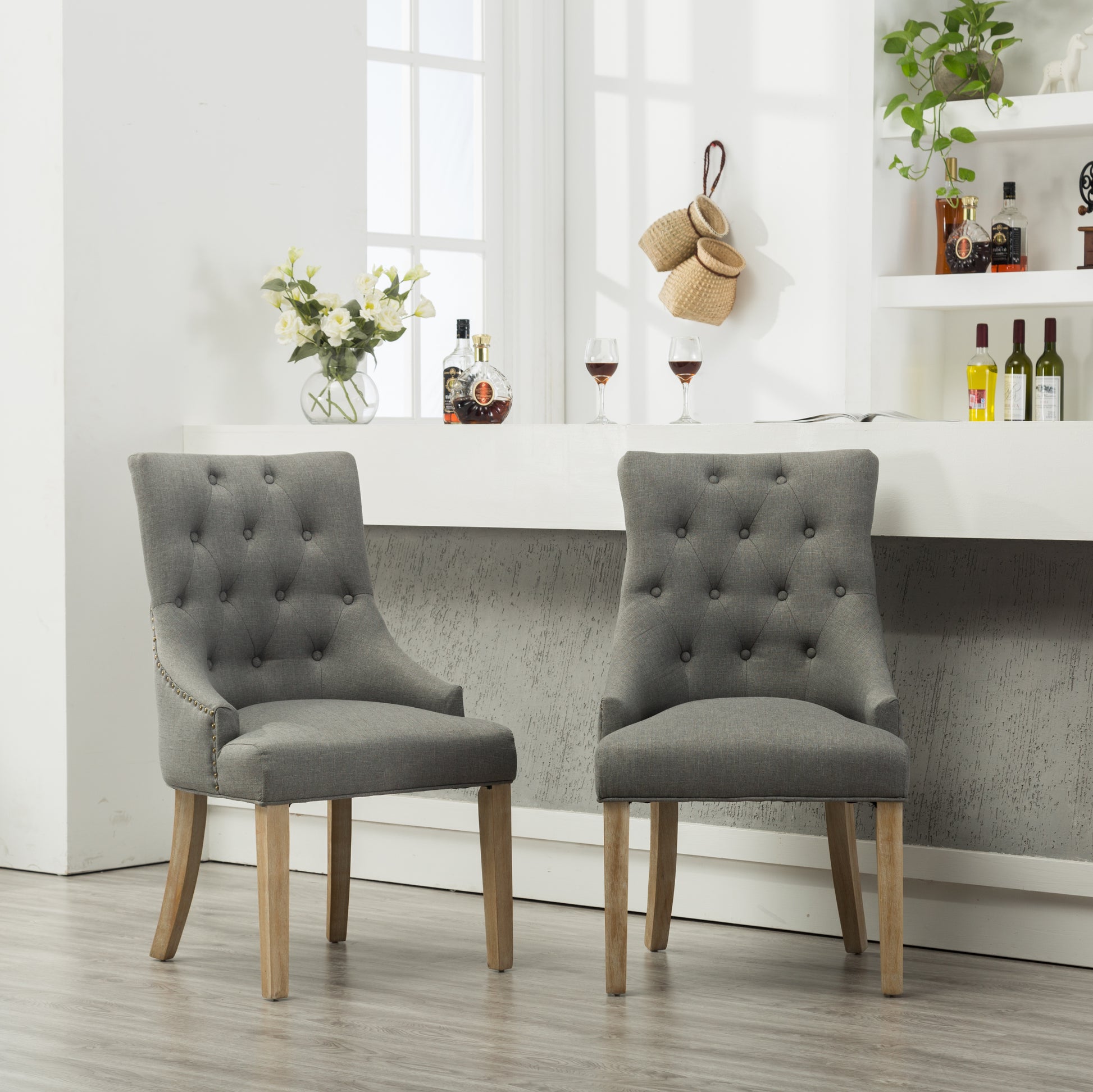 Two grey linen tufted dining chairs with brass nailhead trim and natural wood legs