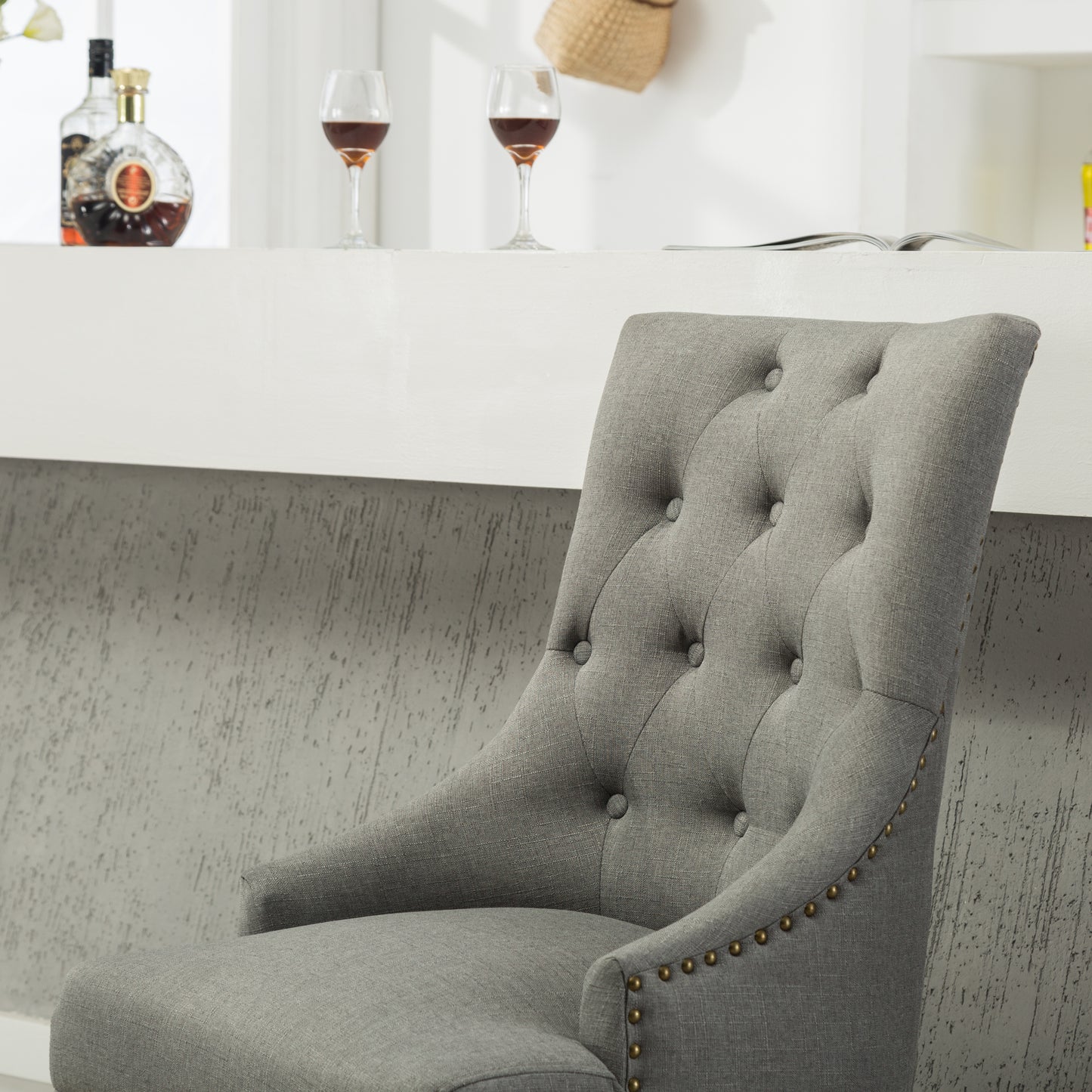 Grey upholstered bar stool with tufted back and brass nailhead trim