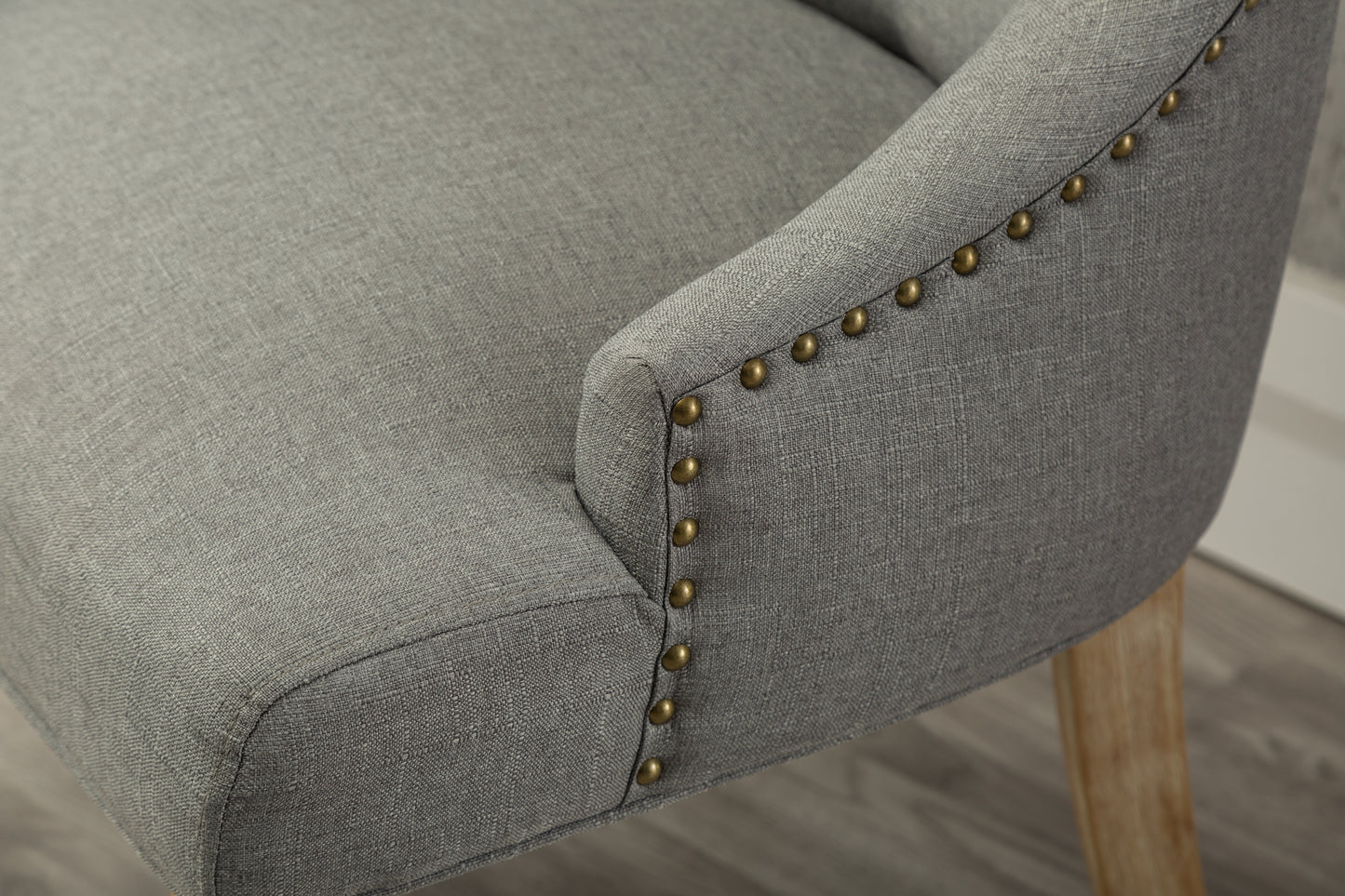 Grey upholstered accent chair with brass nailhead trim and light wood legs