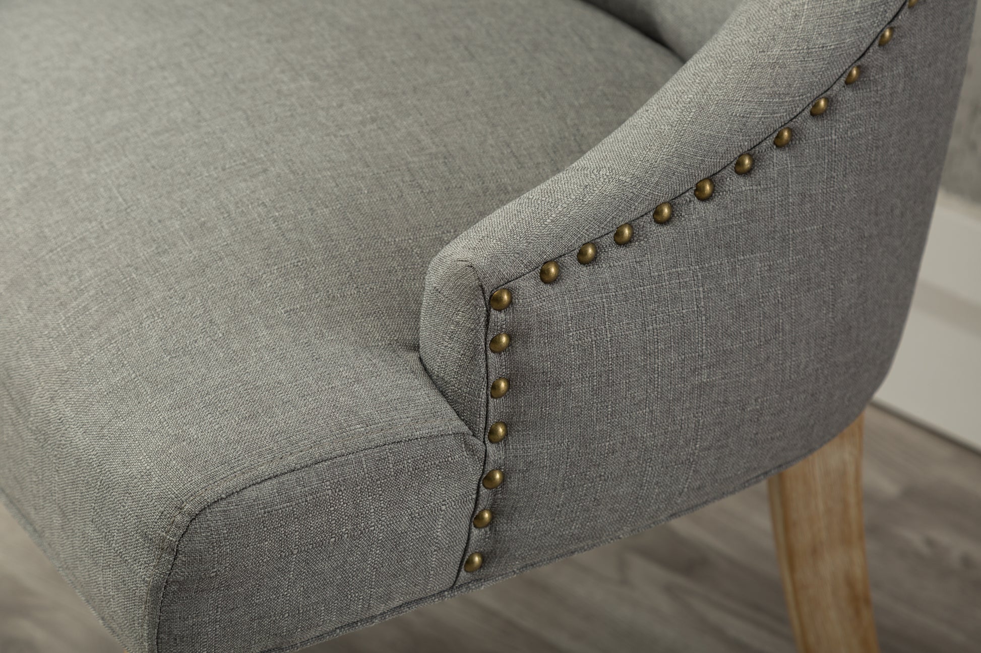 Grey upholstered accent chair with brass nailhead trim and light wood legs