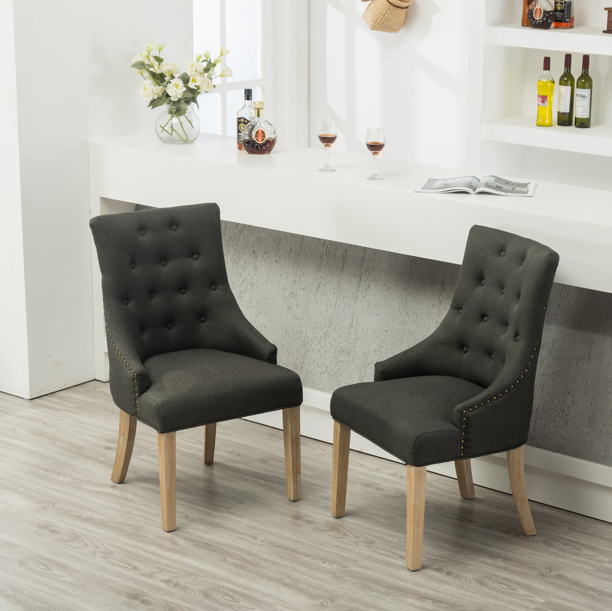 Dark grey upholstered dining chair with button tufting and brass nailhead trim accents