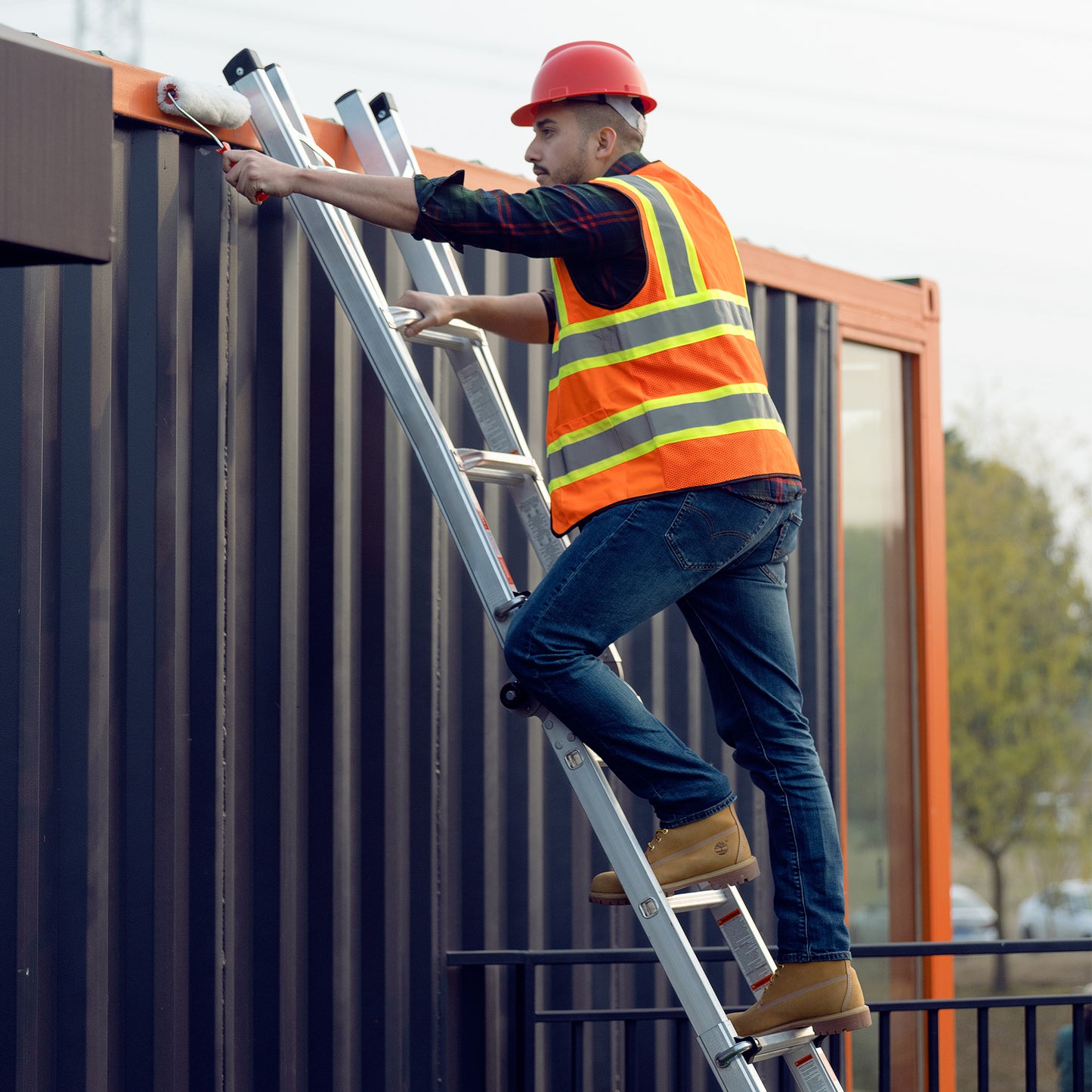 Construction worker in red hard hat painting on a tall ladder