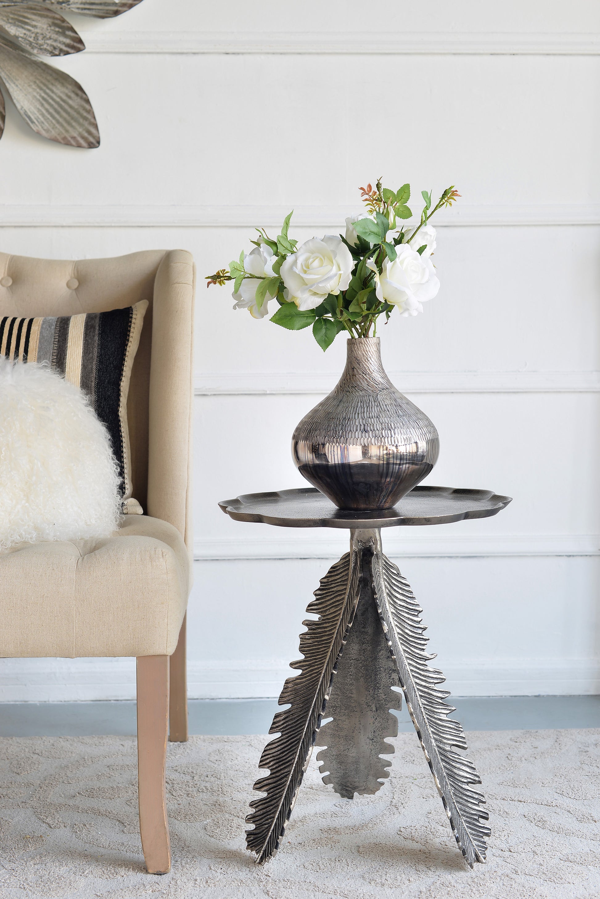 Elegant silver leaf side table featuring a textured metallic vase with white roses
