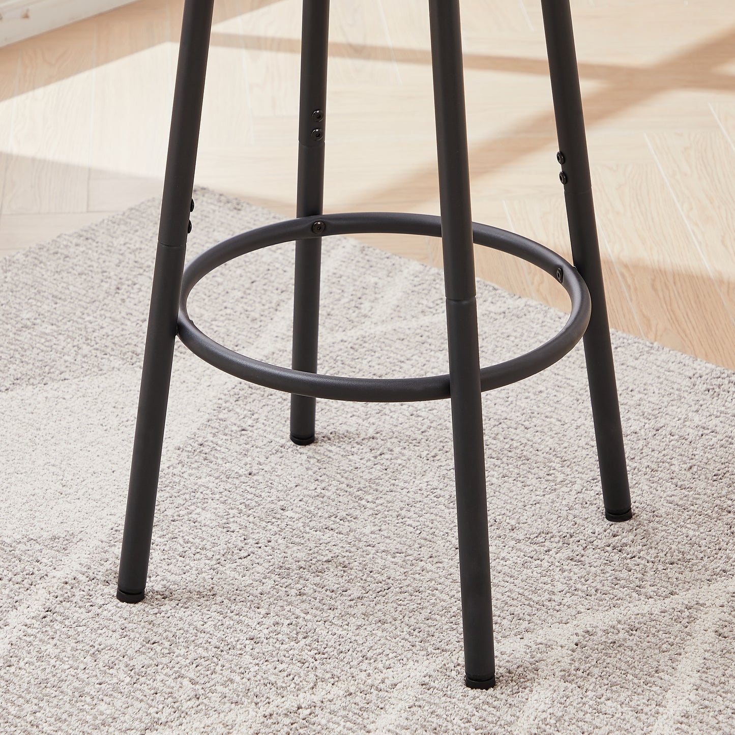 Black metal bar stool legs with circular footrest on textured rug