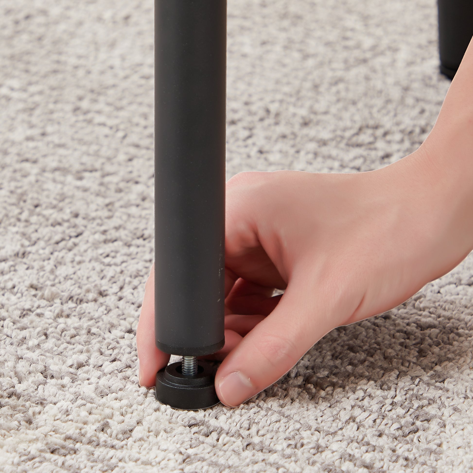 Black metal furniture leg with adjustable leveler being installed on carpet
