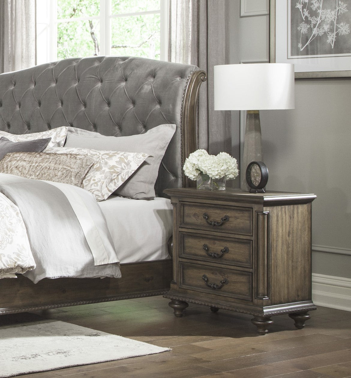 Tufted grey velvet headboard on a wooden bed frame with ornate detailing