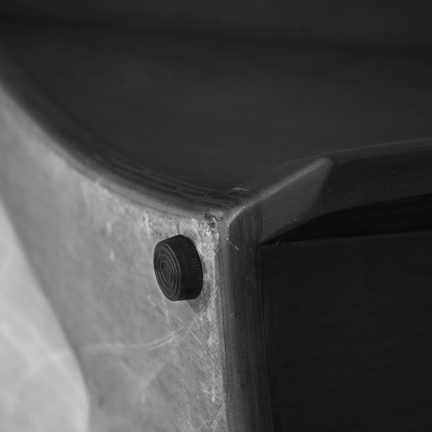 Black threaded foot attached to the corner of a wooden furniture piece