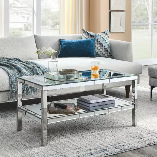 Mirrored coffee table with chrome legs featuring a reflective top and lower shelf for books and decor