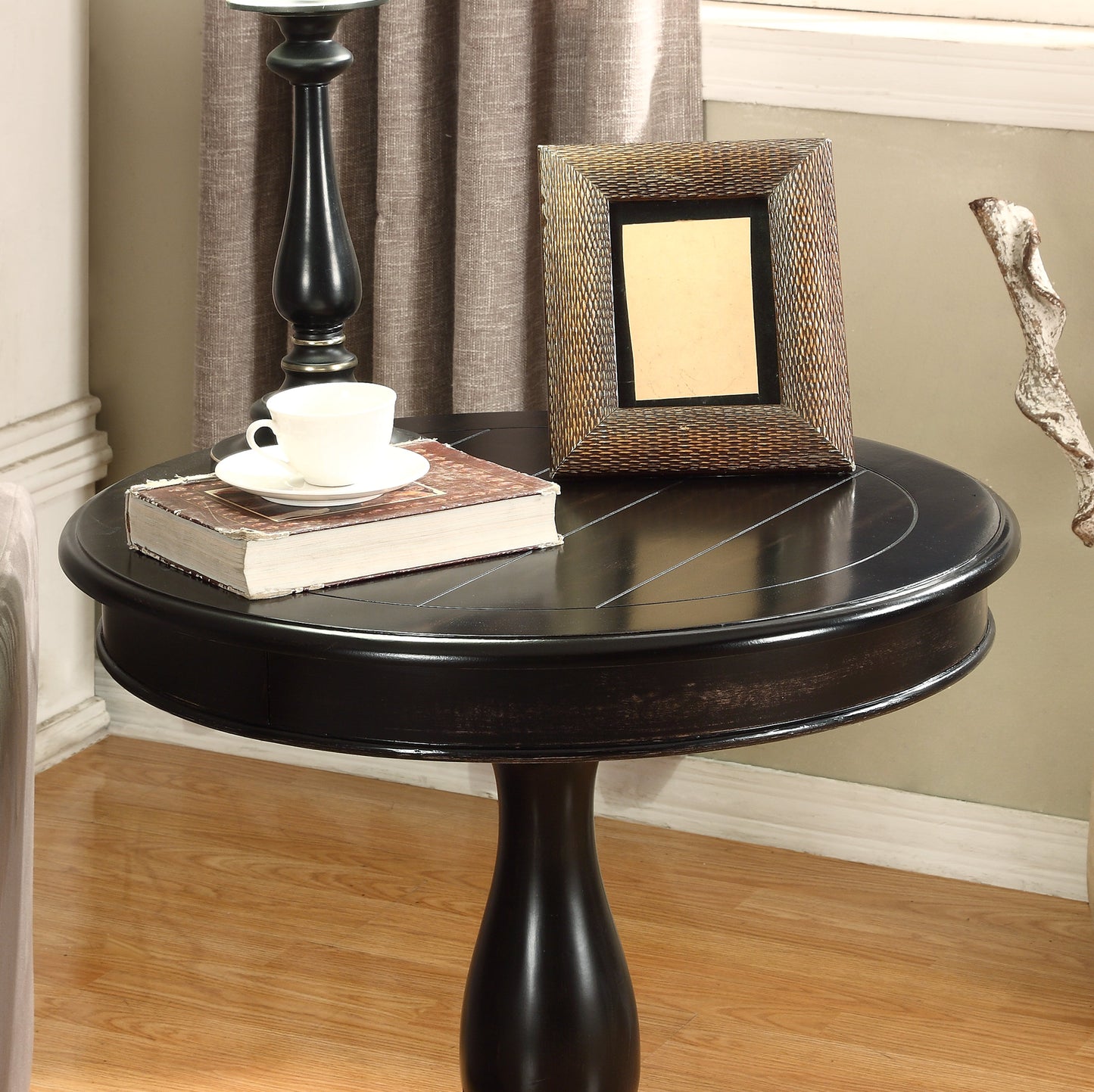 Dark wood pedestal accent table with decorative inlay holding a book and teacup