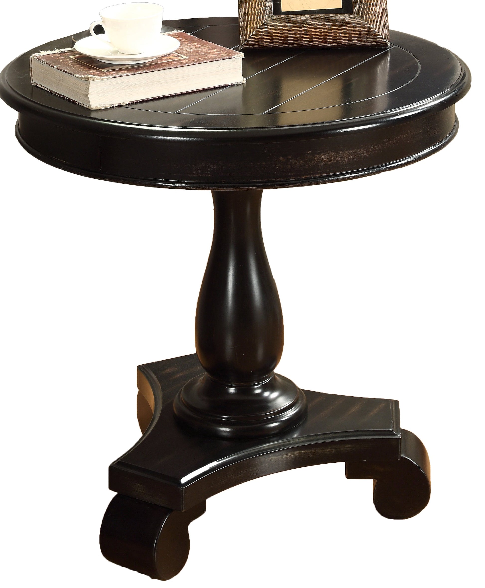 Dark wood round accent table with ornate base holding a book and teacup