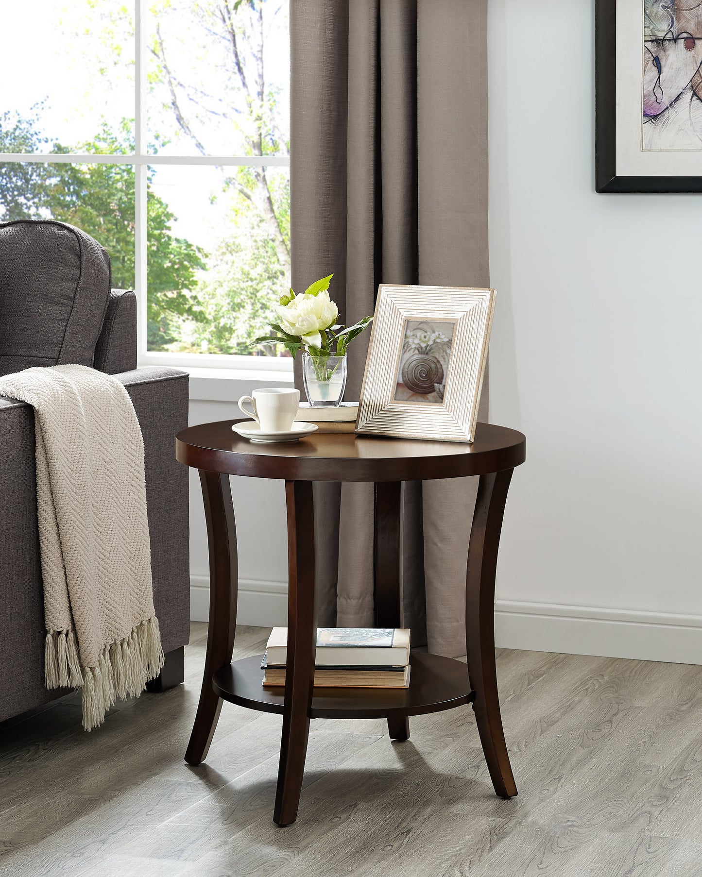 Dark brown round side table with a decorative distressed white picture frame and a white floral arrangement