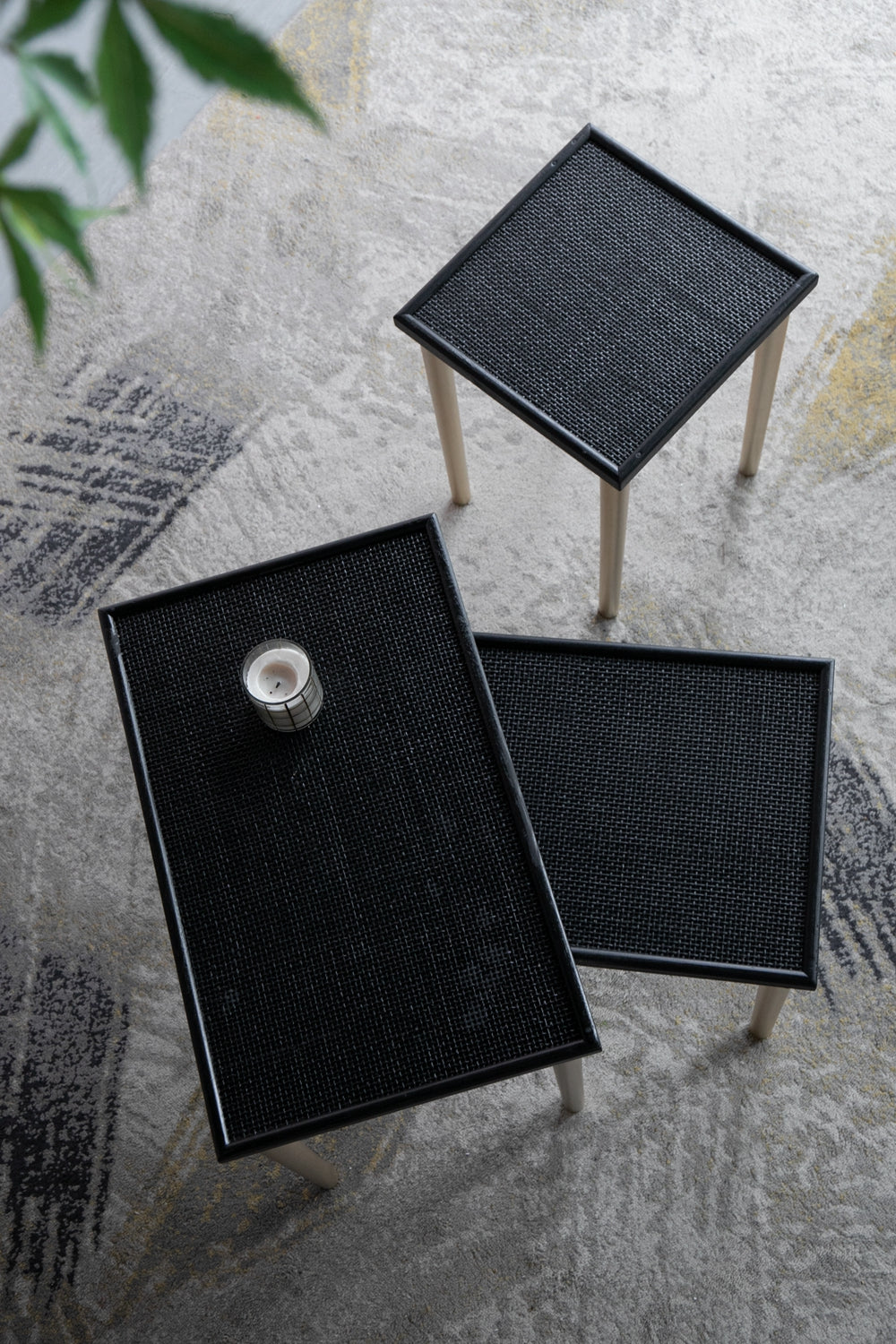 Modern black rattan side table with light wood legs on a textured rug