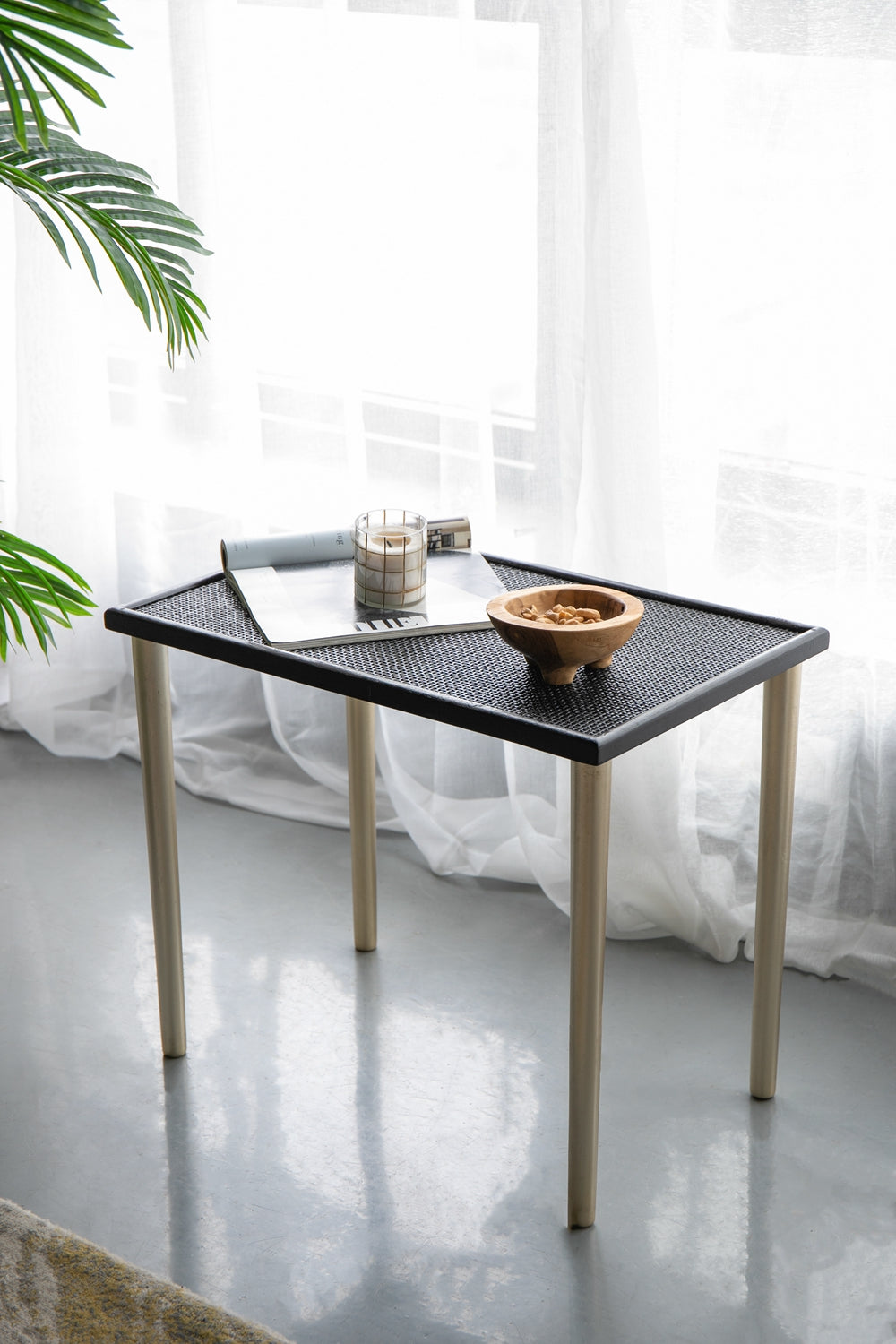 Woven black rattan top side table with natural wood legs holding a candle and bowl of nuts