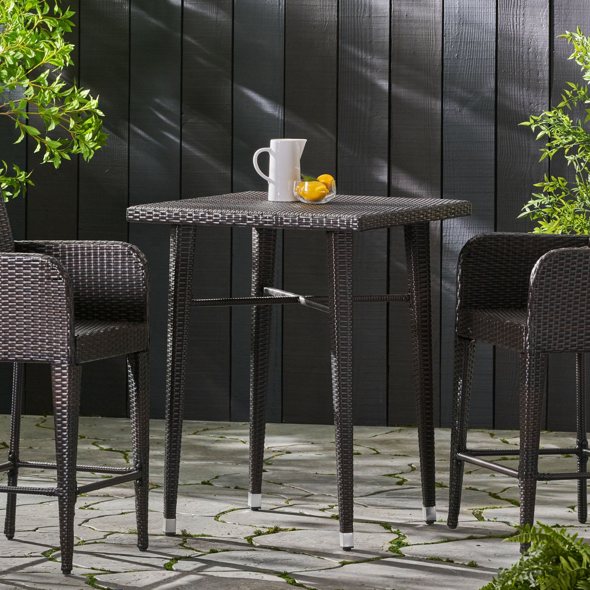 Dark brown rattan bar table with two matching stools on a stone patio