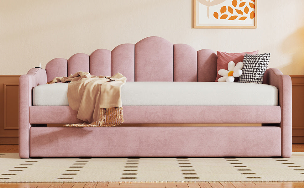 Pink upholstered daybed with scalloped headboard and pullout trundle