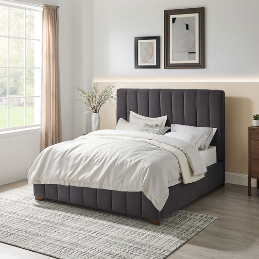 Dark grey upholstered platform bed with vertical channel tufting and plush bedding