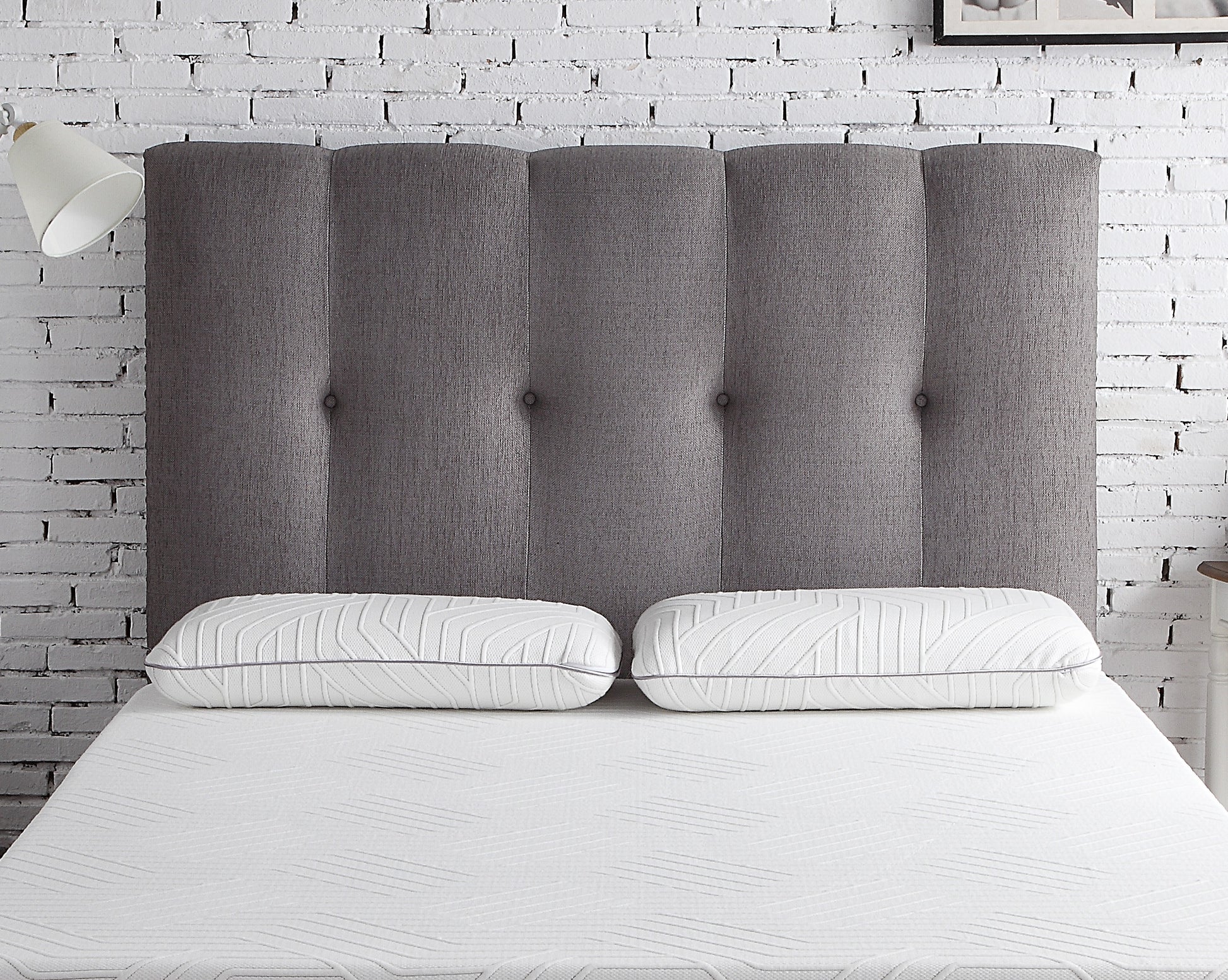 Tufted charcoal grey fabric headboard with channel stitching paired with two white geometric patterned pillows