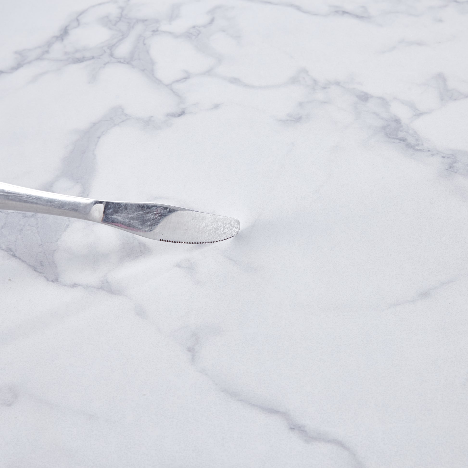 Polished stainless steel butter knife with serrated edge on white marble background