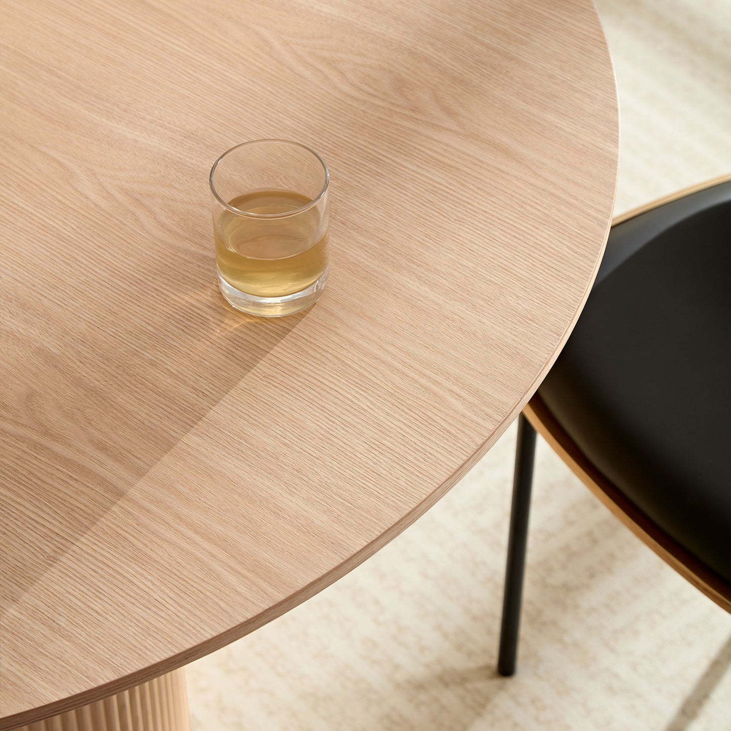 Light oak round dining table with clear glass of beverage minimalist design