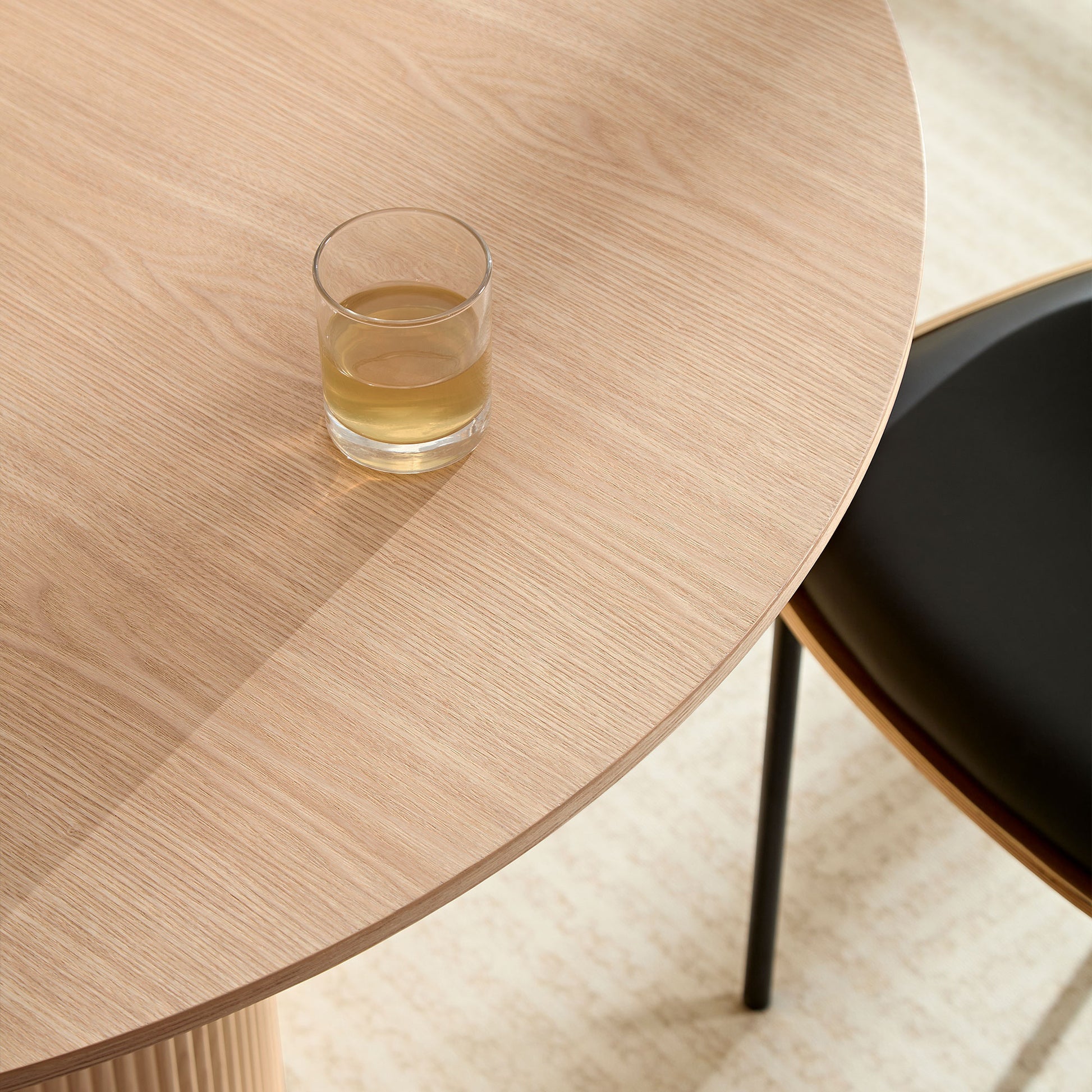 Light oak round dining table with clear glass of beverage minimalist design