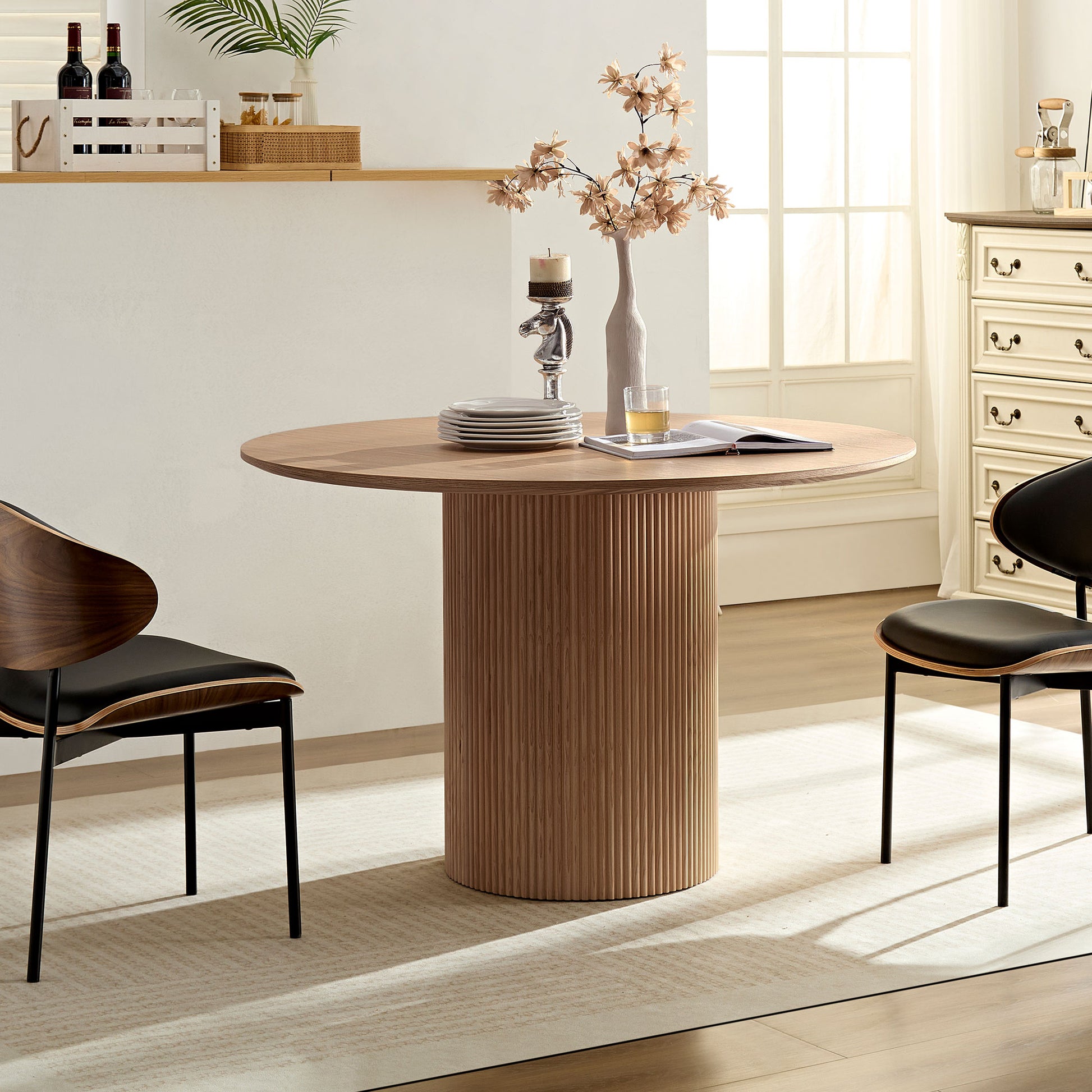 Round wood dining table with fluted pedestal base and two modern chairs