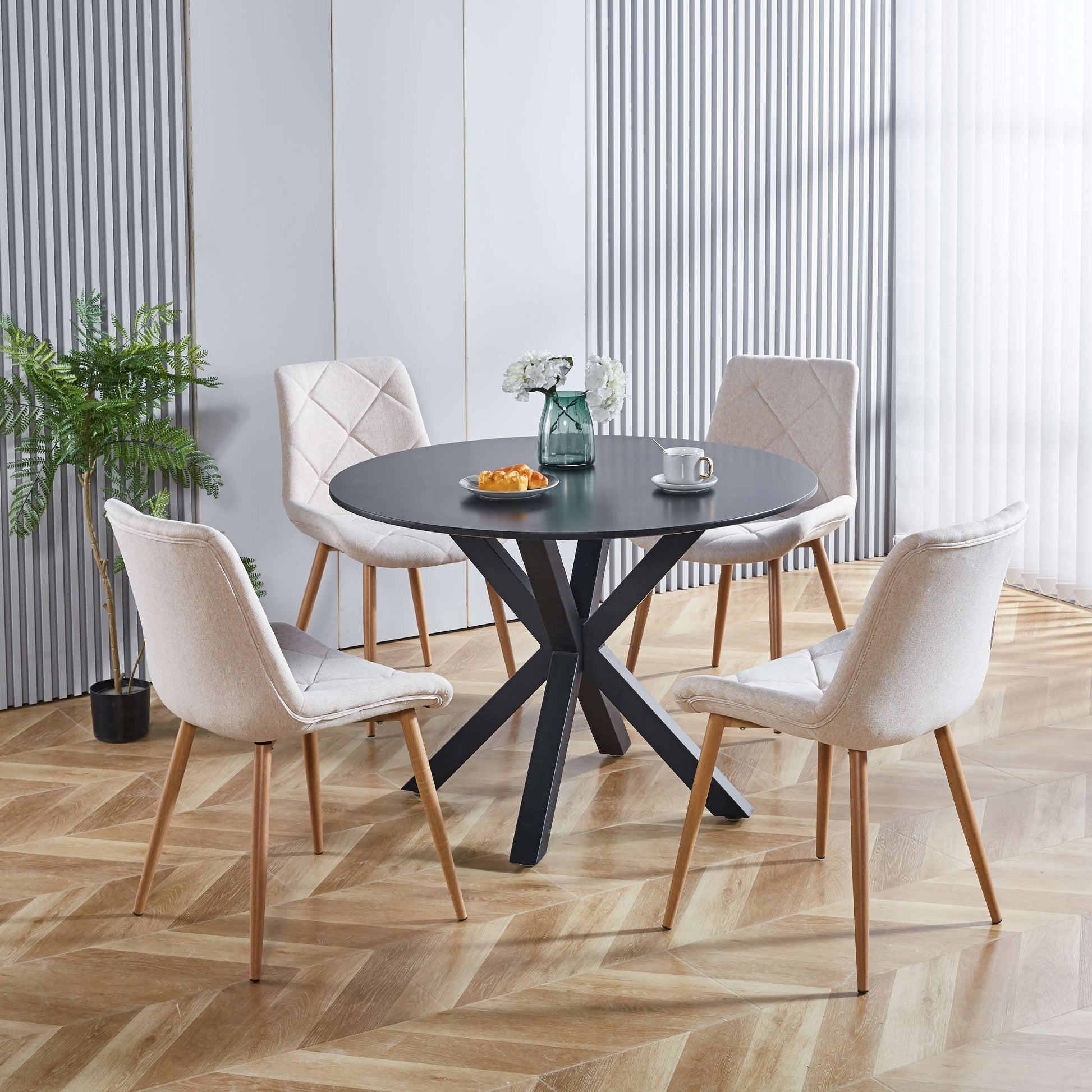 Round black dining table with four light beige upholstered chairs in a modern dining room
