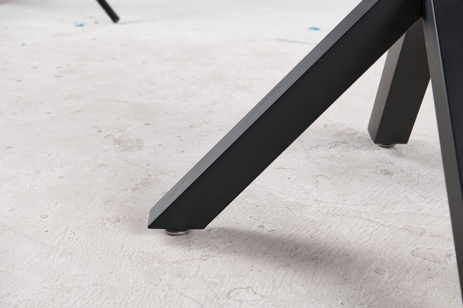Black metal table leg with adjustable foot on textured floor