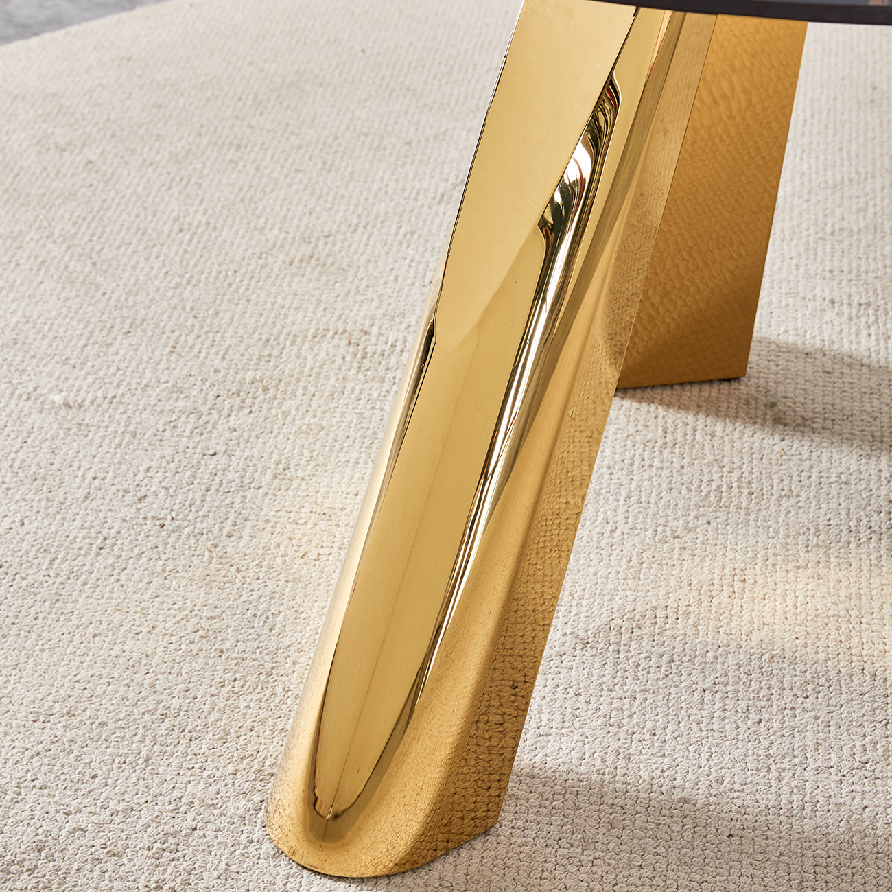 Polished brass table leg with a textured gold support on a cream rug