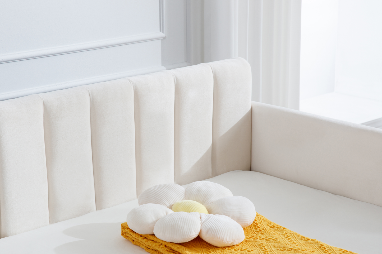 Cream velvet crib with white flower pillow and yellow knit blanket